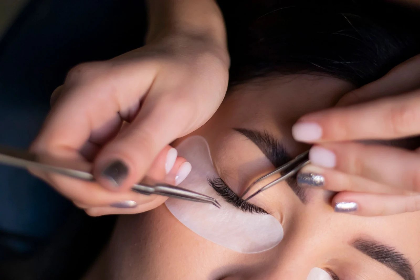 Beauty technician applying false eyelashes to client's eye with tweezers