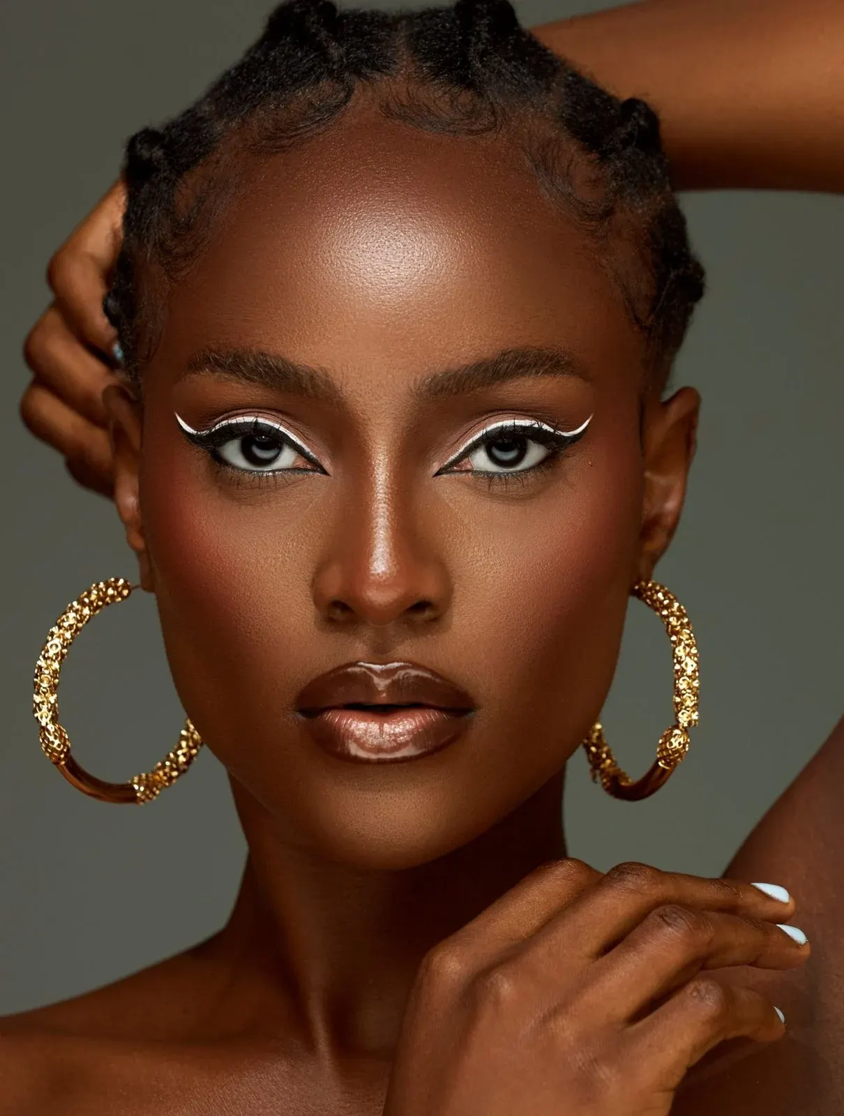 Woman with gold hoop earrings and white eyeliner makeup looking directly at camera