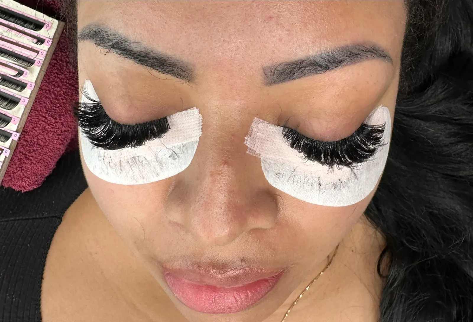 Woman wearing false eyelashes with white under-eye patches during lash application
