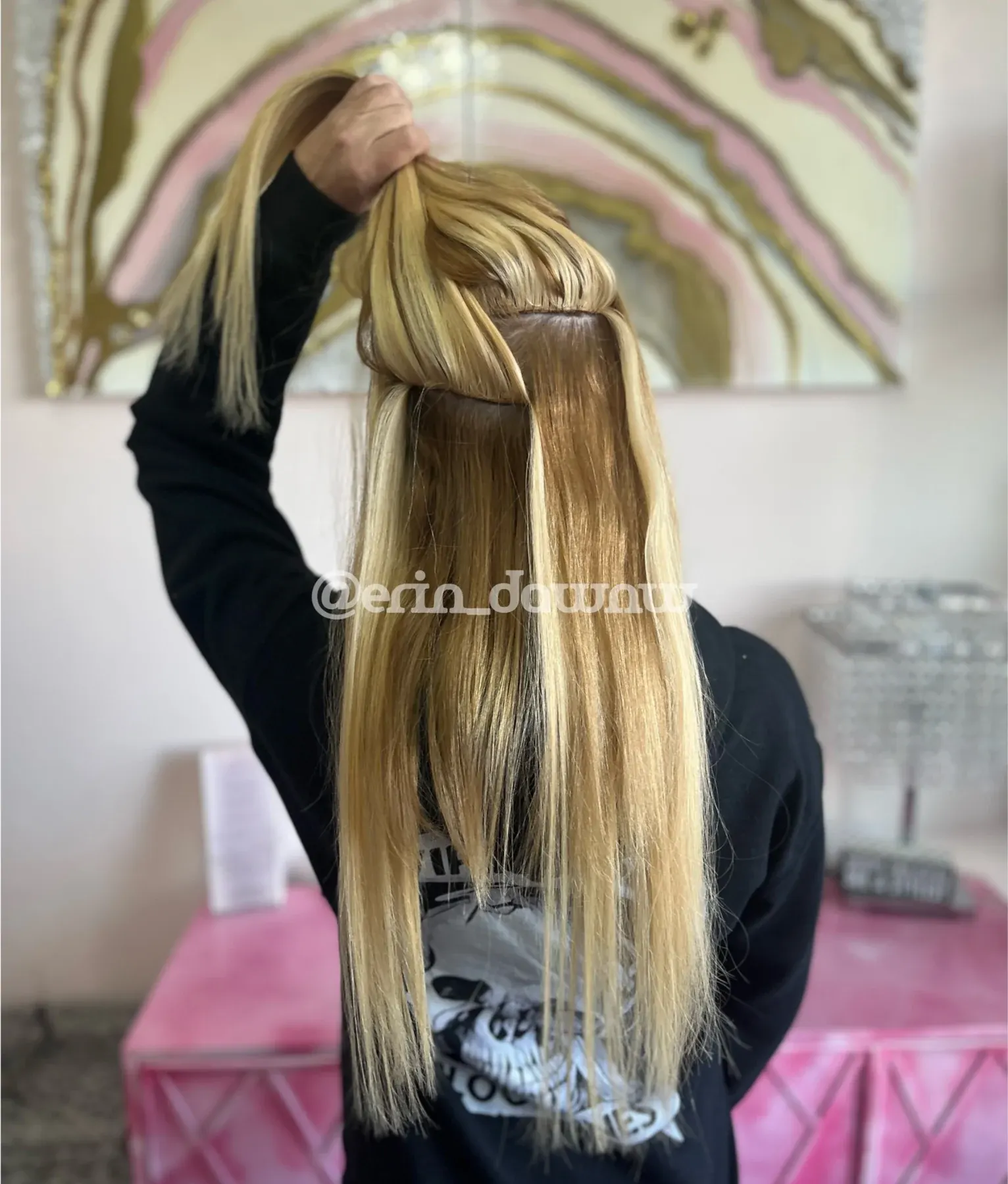 Blonde hair extensions held up by hand, showing length and quality in salon setting