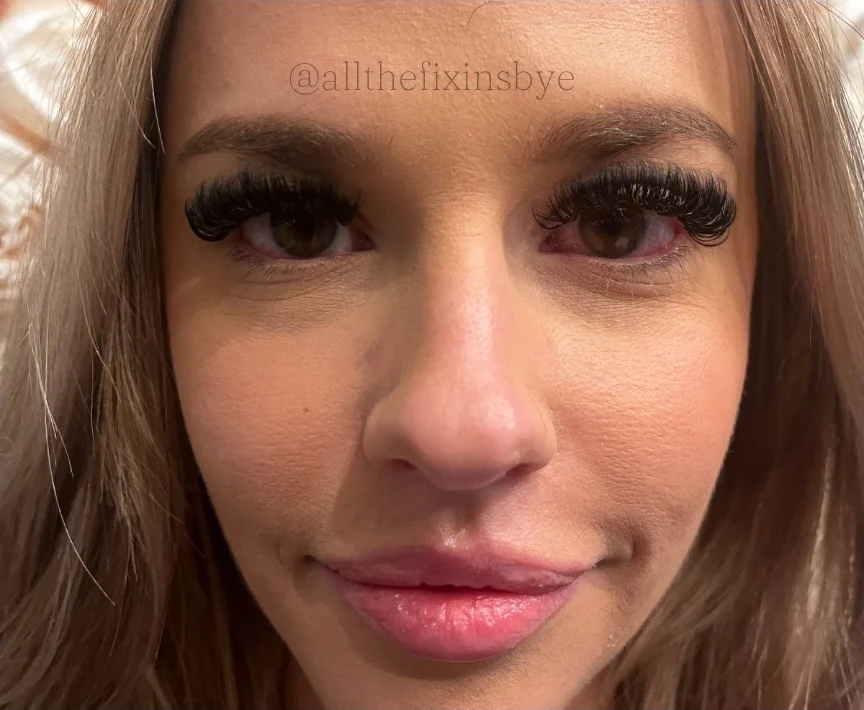 Close-up of a woman's face with long blonde hair, dark eye makeup, and defined eyelashes