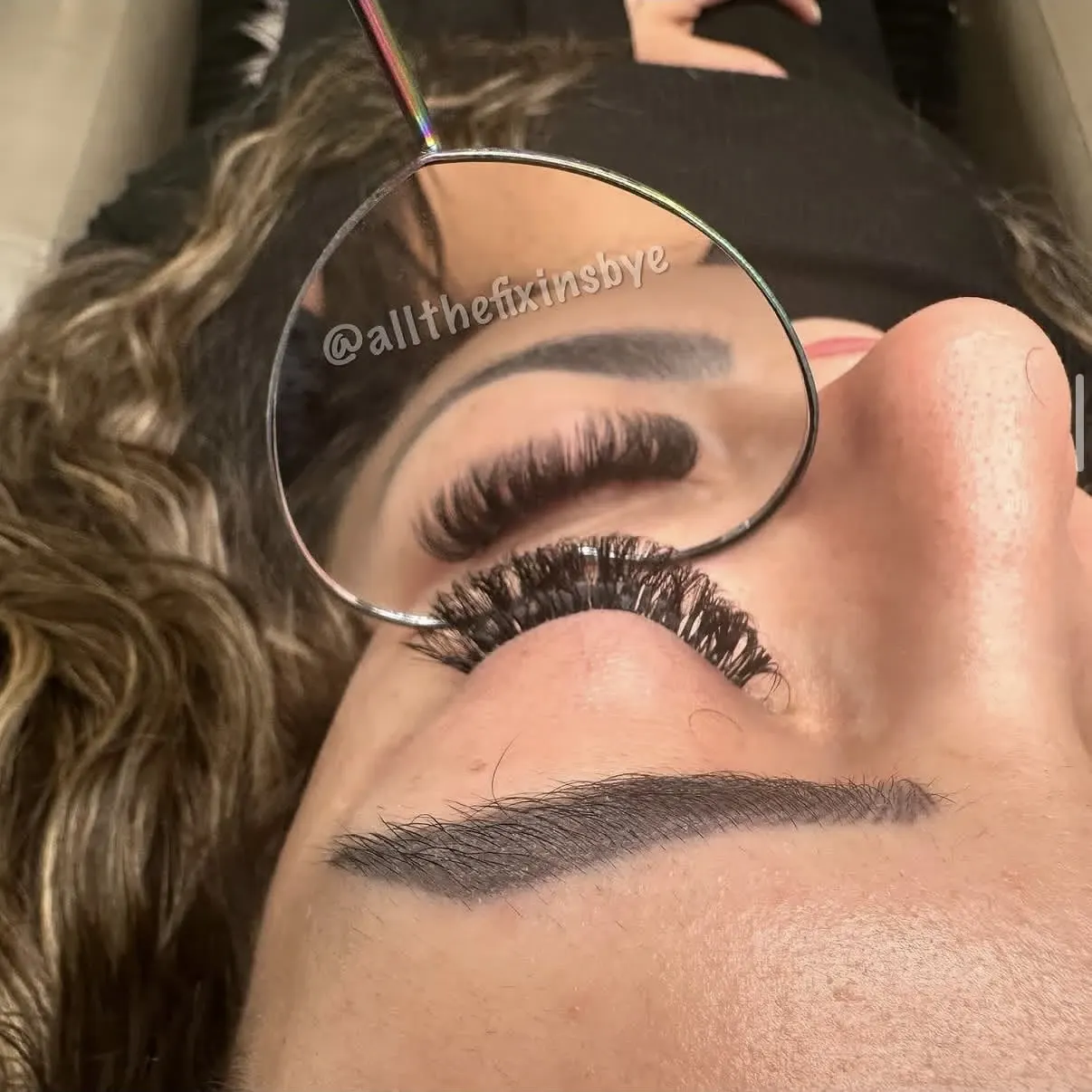 Woman displaying false eyelashes with mirror reflection showing eye makeup application