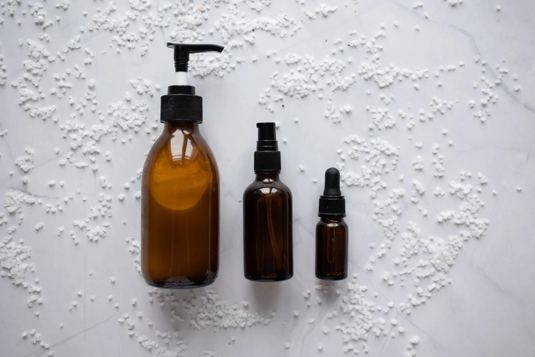 Three amber glass bottles with black dispensers on white textured background